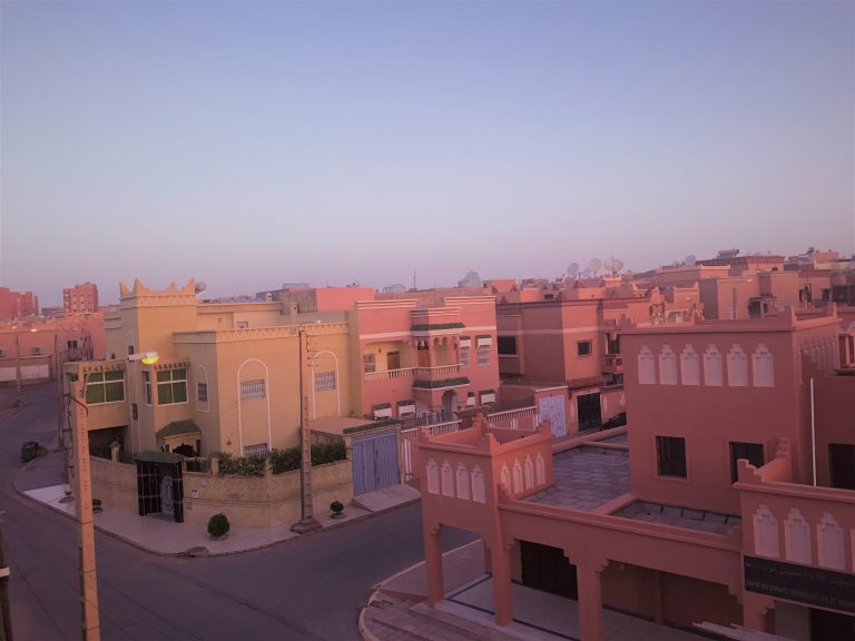 Faint morning blue sky and bright red building of A faint sun over the red houses of Ouarzazate