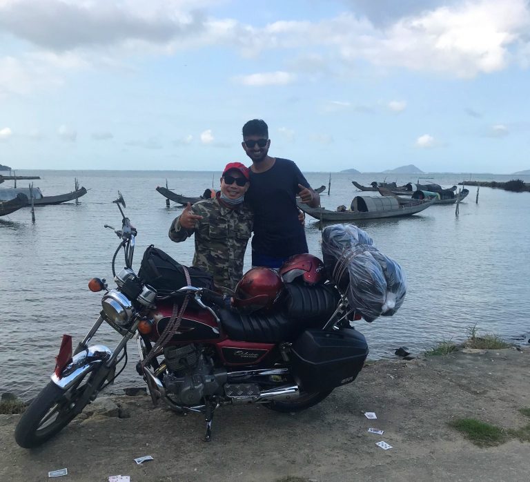 Chao and Nishil Stand behind Motorbike in a fishing village