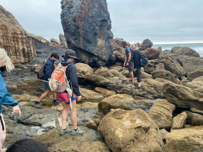 Hiking group hikes through the boulders along the coast