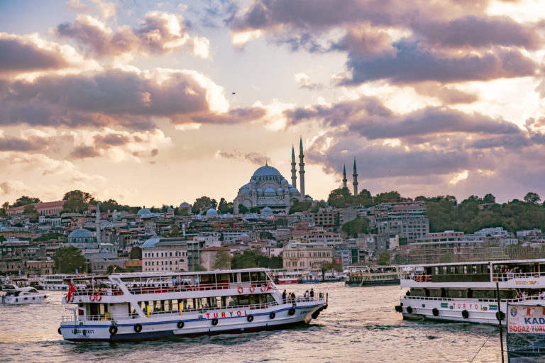 Boats pass by as the sun sets behind a mosque